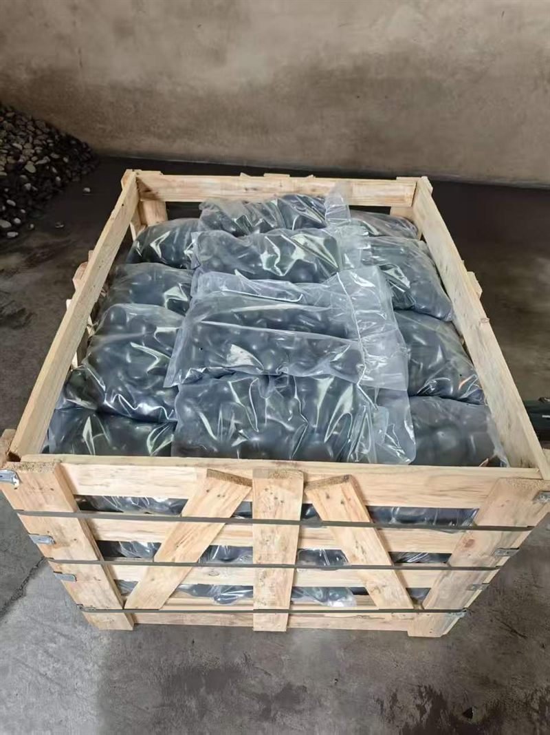 Transparent retail bags of black pebbles packed in an open wooden export crate