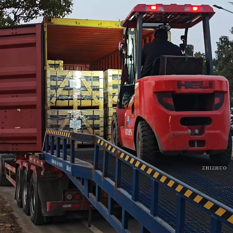 A forklift loading strapped wooden crates of stone into a shipping container from a loading ramp