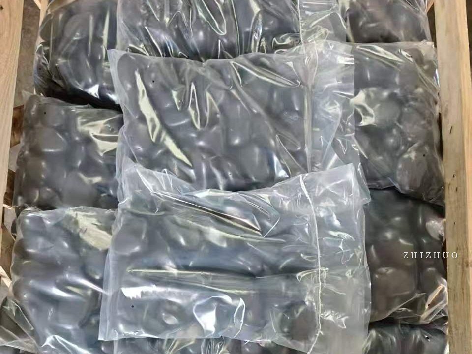 Black polished pebbles packed in transparent bags inside a wooden export crate
