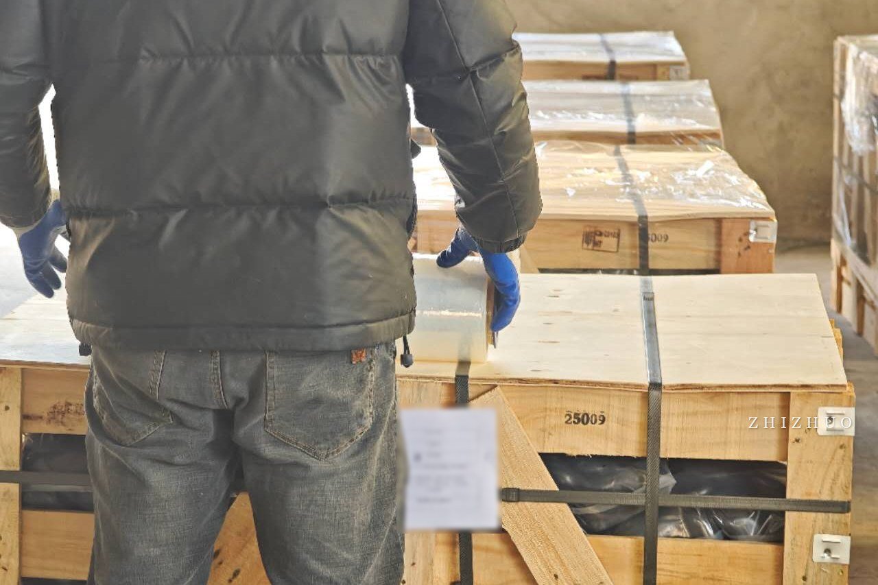 A worker wrapping and checking a strapped wooden crate of stone before export loading